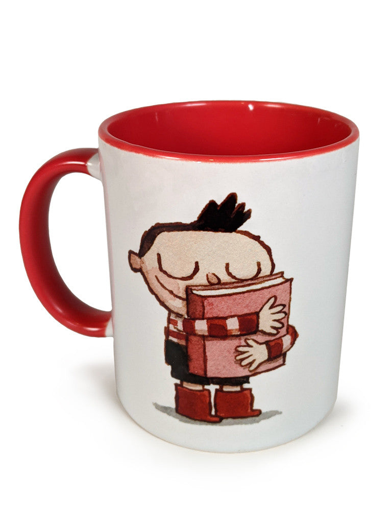A Spoke Art white mug with a red handle and interior, featuring an illustration of a smiling child with closed eyes hugging a red book.