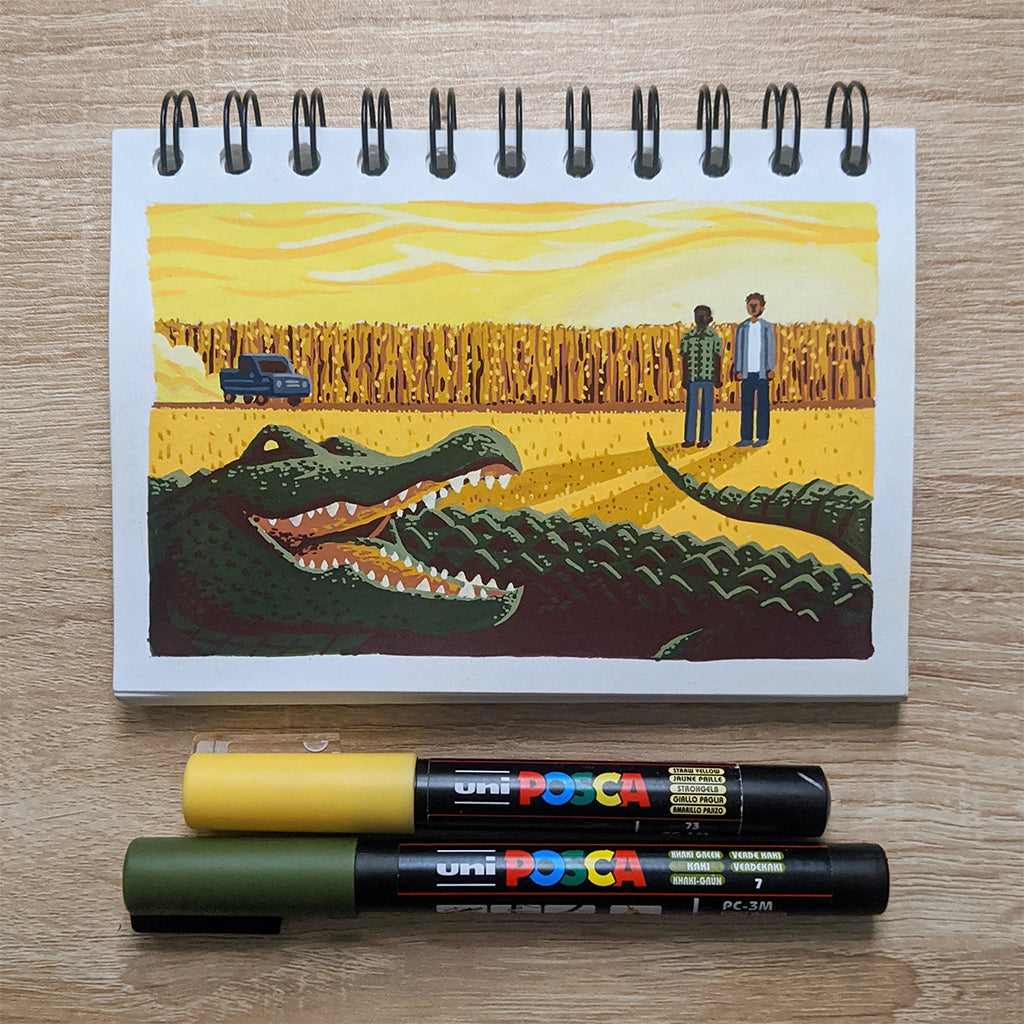 A James Chapman spiral notebook showcases a large crocodile facing two people and a car in a rural setting. Yellow and green Posca markers lie beneath it, evoking the ambiance of Nickel Boys and reminiscent of cover art from Spoke-Art.com.