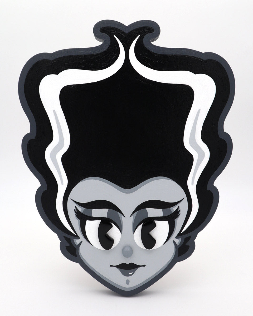Stylized cartoon portrait of a woman with a tall, black beehive and white streaks, acrylic on wood. She has large eyes, long lashes, red lips, and a gray face on a white background. By Miles Ritchie for Spoke Art's 15th Anniversary Show.