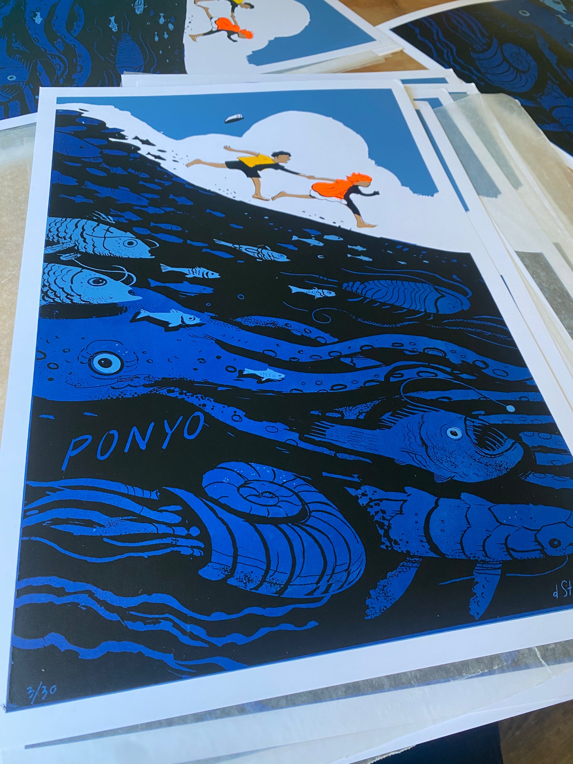 A vibrant Dean Stuart screen print shows two children running over the sea, diverse ocean life below, and "PONYO" underwater. Blue tones with orange highlights celebrate Spoke Art's 15th Anniversary.