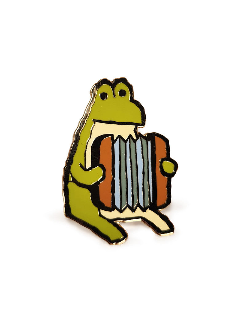 Scott C. limited edition hard enamel pin featuring a green frog sitting upright and playing an accordion with a neutral expression. Gold metal plated with a white background, presented in charming cartoon style.