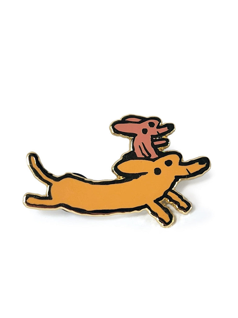 A playful Scott C. hard enamel pin of two cartoon dachshunds—one orange, one pink—happily running. Outlined in black on white with gold plating.