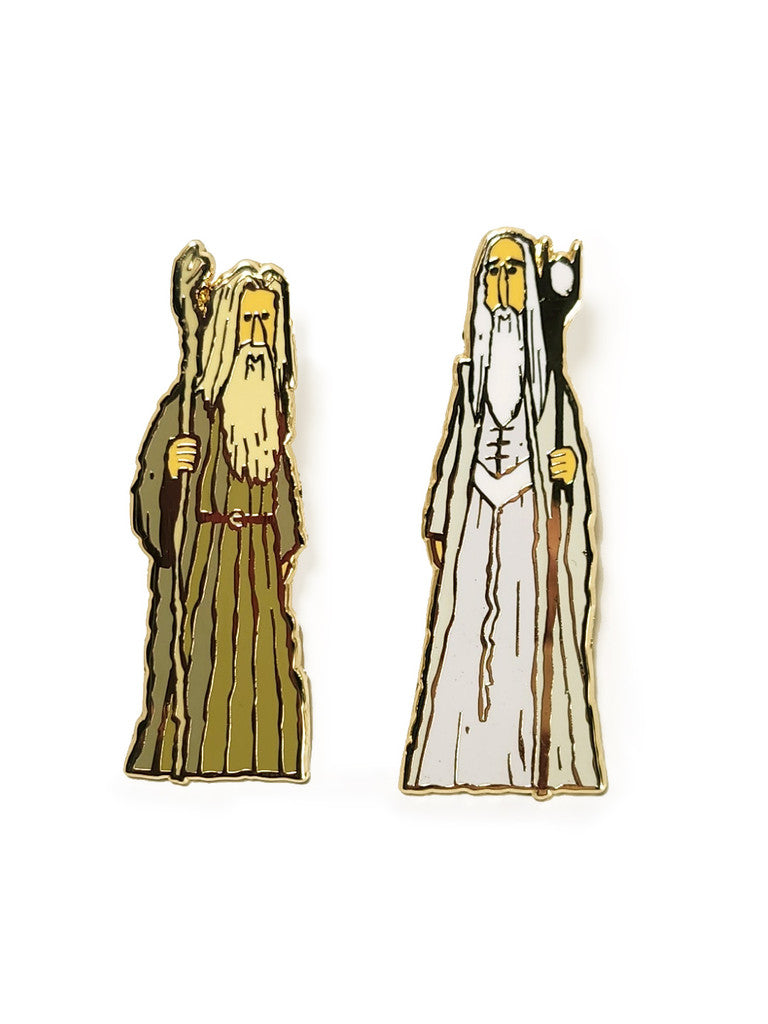 Scott C. presents two gold metal plated hard enamel pins featuring cartoon wizards with long white beards and staffs—one in a brown robe, one in a white robe—both set against a white background.