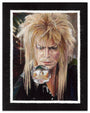 With wild blonde hair, a person holds a reflective crystal ball, capturing an upside-down figure inside. The dark backdrop enhances the vibrant scene, resembling an archival pigment print. Brand: Rose Couch.