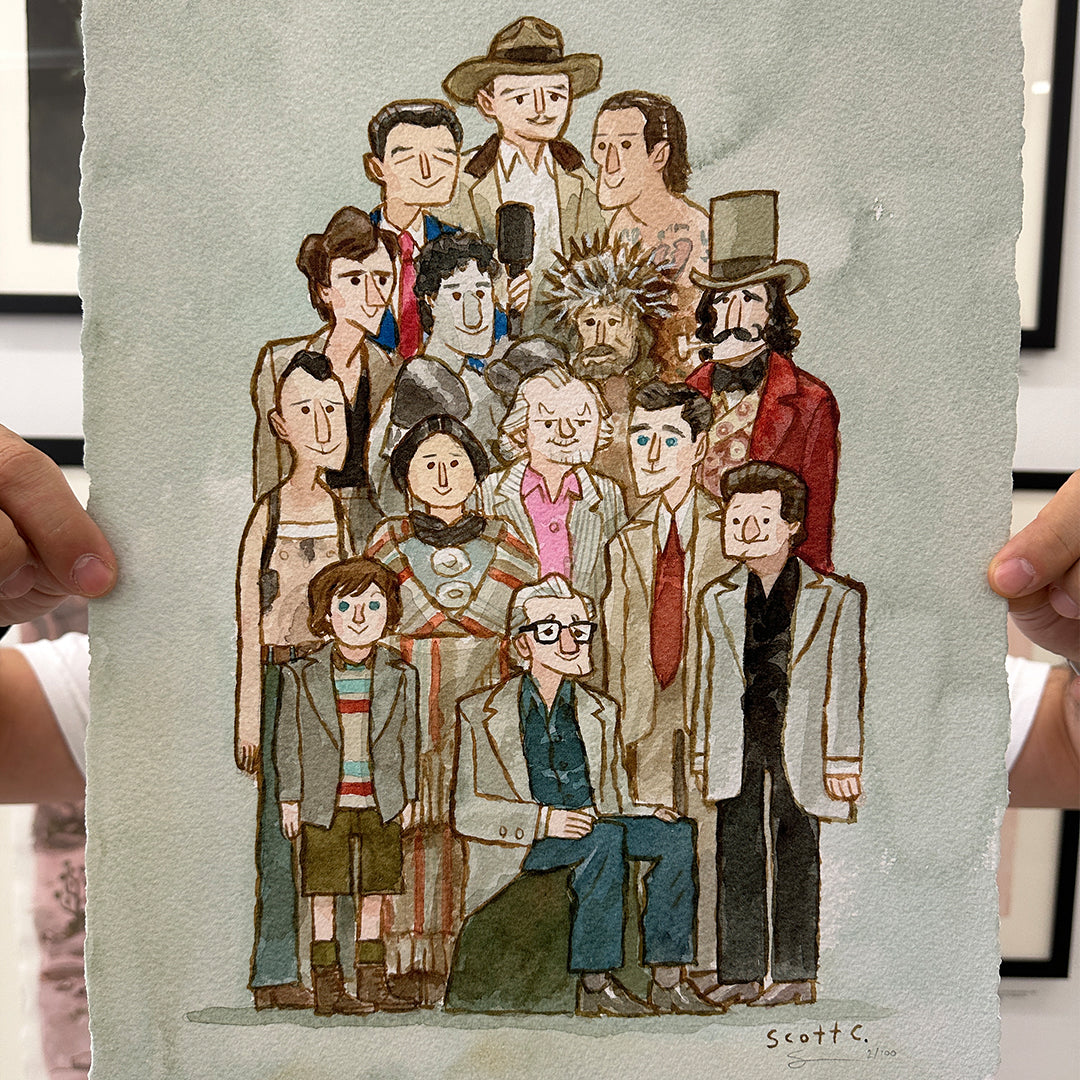 A person holds up a limited edition Scott C. drawing featuring uniquely dressed characters with distinctive hairstyles, standing and sitting together against a light green background. The artwork is hand-signed by the artist.