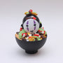 A black bowl by Zard Apuya holds a No-Face-inspired figurine, resembling a Kidrobot Munny vinyl toy, topped with colorful accents to create playful No Face Carne Asada Fries—a unique fusion designed for San Diego Comic-Con 2025.