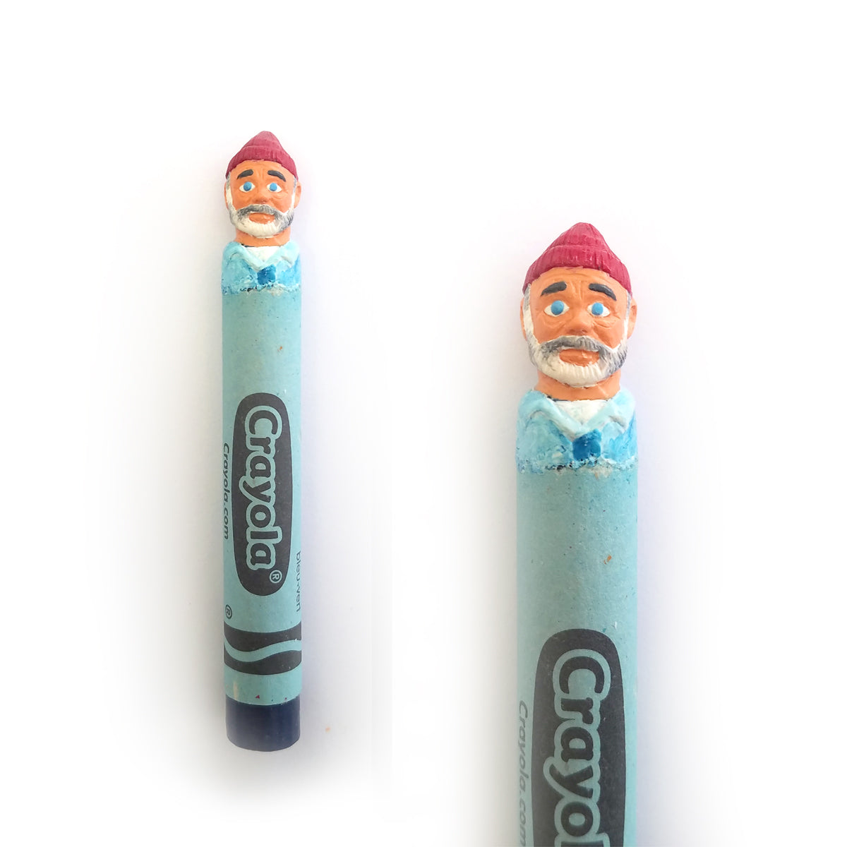 This light blue, hand-carved Crayola crayon by Hoang Tran features a detailed sculpture of a man with a white beard, red beanie, and blue shirt at the tip. Viewed from two angles, it captures artistry reminiscent of The Life Aquatic.