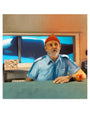 A man in a blue shirt and red beanie sits at a counter with an apple beside him, against a backdrop of an underwater scene featuring a whale. The setting captures the warm, nostalgic feel of a Kemi Mai archival pigment print.