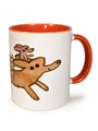 A Spoke Art white ceramic mug with an orange handle and interior, featuring Scott C. art of two brown cartoon dogs running as a smaller pink dog rides playfully on the larger dogs back.