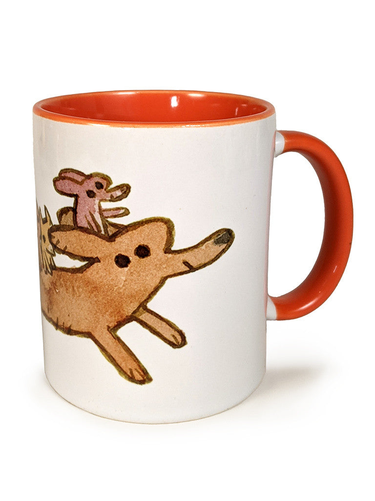 A Spoke Art white ceramic mug with an orange handle and interior, featuring Scott C. art of two brown cartoon dogs running as a smaller pink dog rides playfully on the larger dogs back.
