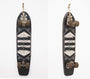 A vintage GATS skateboard features a black deck with an abstract white geometric design, like acrylic art. Wooden and worn, its scuffed brown wheels hang vertically on a white wall, capturing the eclectic essence of Art Market San Francisco.