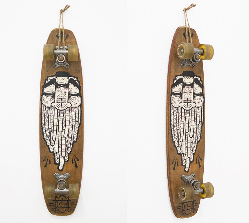 A GATS-designed longboard hangs vertically against the wall, featuring a wooden deck with an acrylic illustration of a bearded face. Retro-style wheels and metal trucks complete this Artisan Market San Francisco-inspired vintage piece.