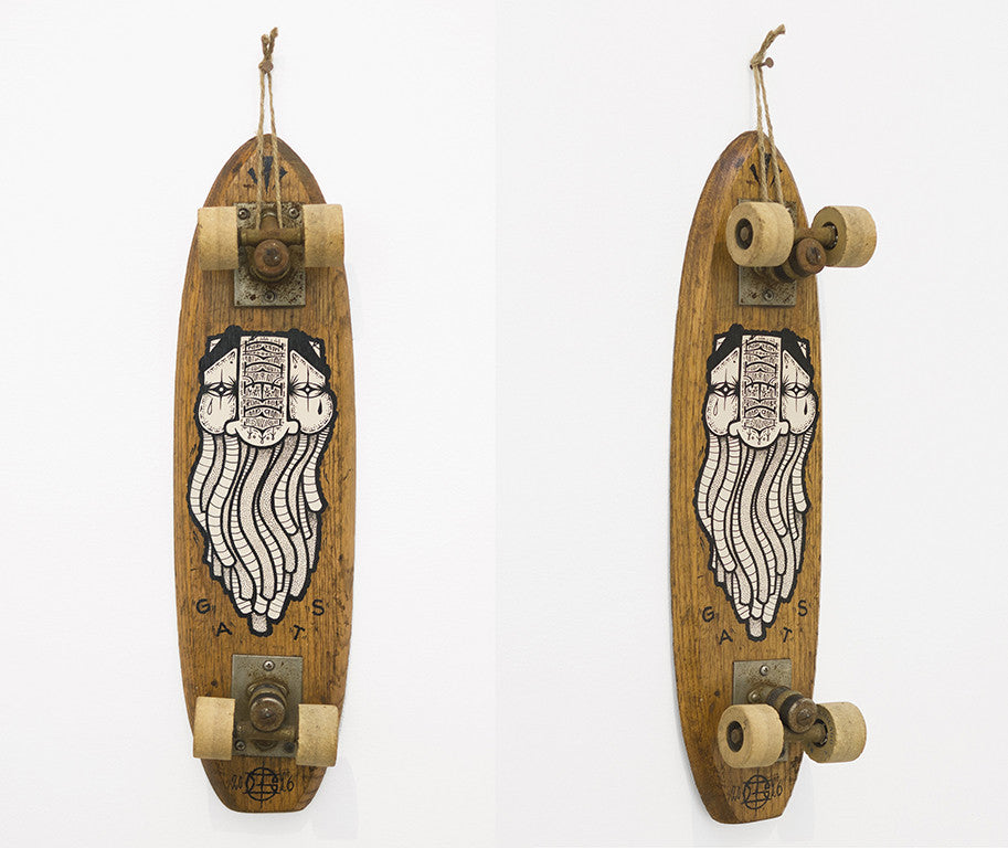 This vintage wooden skateboard, featuring a GATS graphic of a bearded man in a helmet, displays white wheels and hangs vertically on the wall. Its rustic charm makes it perfect for any Art Market San Francisco collection as an acrylic art example on vintage skateboards.