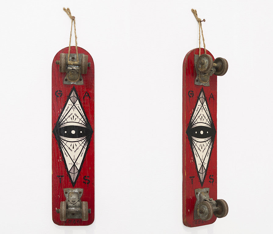 A GATS vintage skateboard art piece, mounted vertically on the wall, features a red deck with a striking black and white eye design in a diamond shape. It includes metal parts at the top and bottom and a rope loop for hanging, making it an intriguing addition to any San Francisco art market.