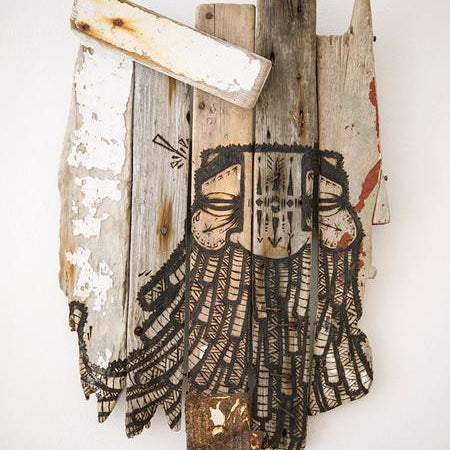 A GATS wooden art piece showcases a bearded face painted on weathered vertical planks. Resembling burnt driftwood, it features varied shades, textures, accented with white paint, and intricate black line details highlighting the facial features and beard.
