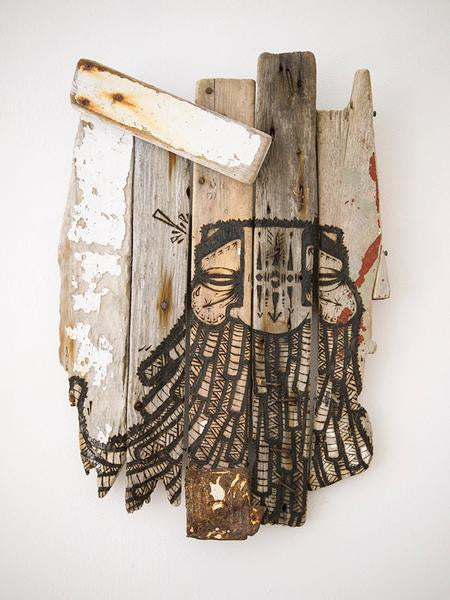 A GATS wooden art piece showcases a bearded face painted on weathered vertical planks. Resembling burnt driftwood, it features varied shades, textures, accented with white paint, and intricate black line details highlighting the facial features and beard.