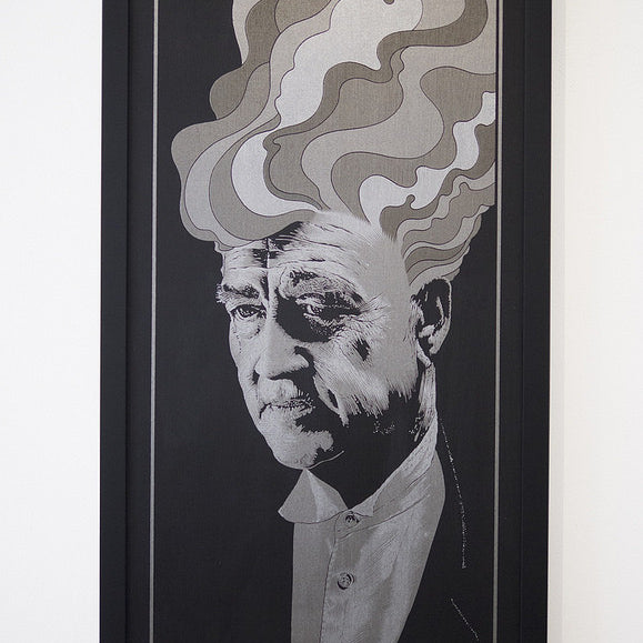 A framed Chuck Sperry artwork features a portrait with stylized, swirling smoke shapes from the persons head. The monochromatic palette of gray, black, and white evokes David Lynchs cinematic style, amplifying its dramatic effect.
