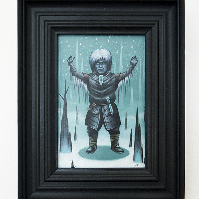 A framed artwork by Jeff McMillian shows a fantasy character with white hair in a dark tunic and boots, standing in a snowy landscape with raised arms, surrounded by jagged ice formations. Exhibited at Spoke Art gallery, it evokes the essence of blue.