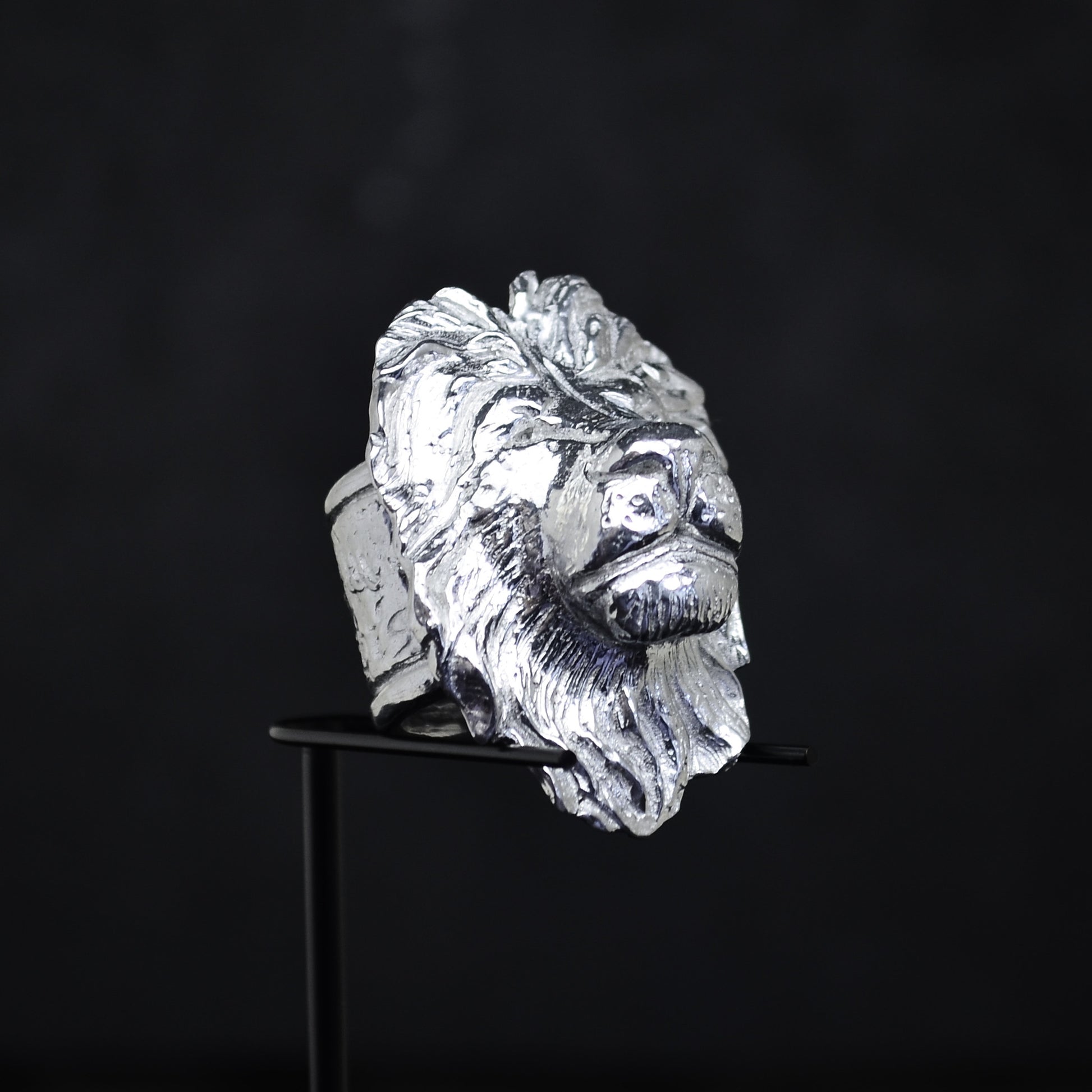 The Rebecca Rose silver ring, crafted as a roaring lions head, is elegantly displayed beneath a hand-blown glass dome. Its detailed mane and facial features give it a bold appearance against the dark background.