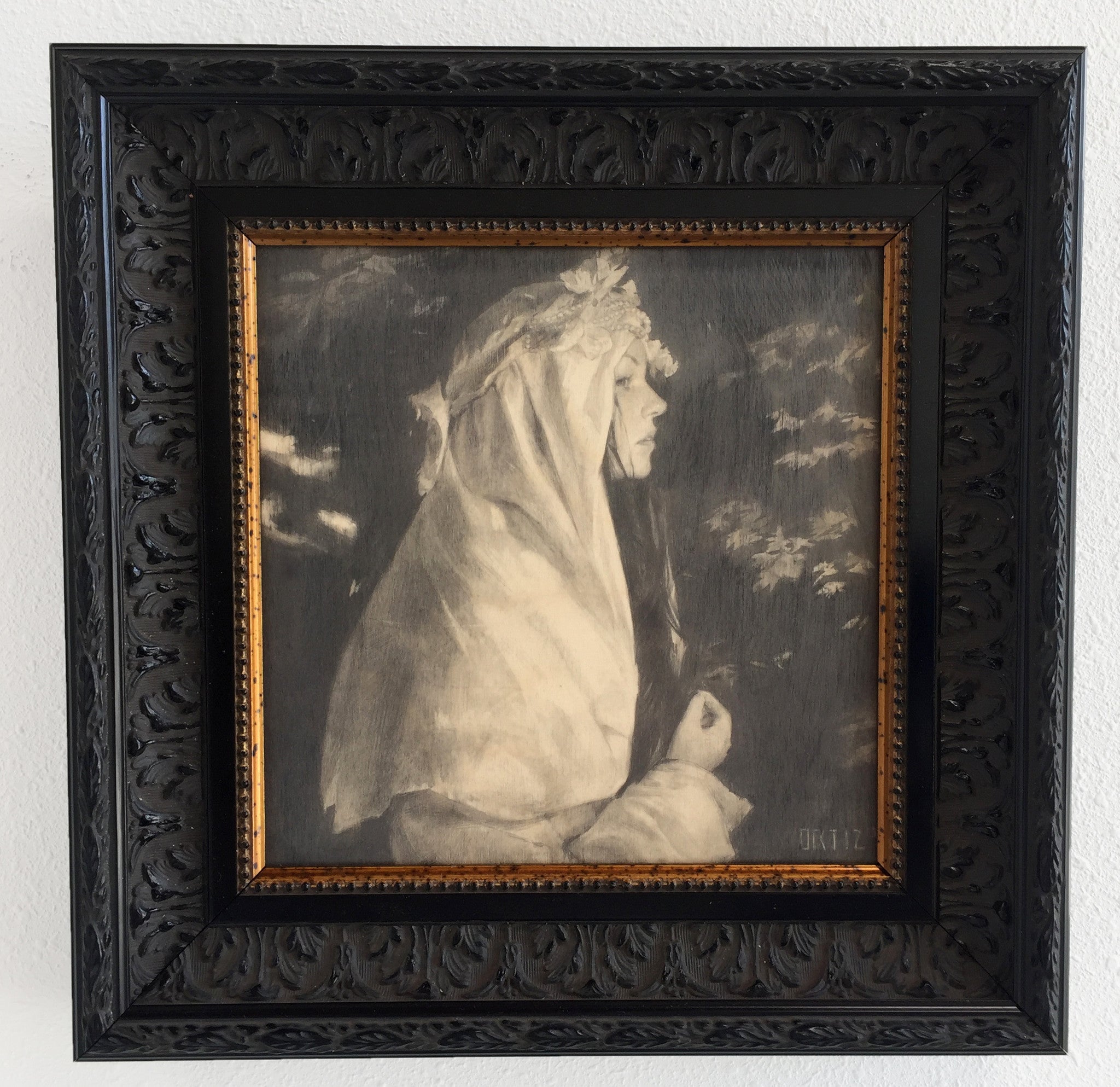 La Cura by Karla Ortiz is a black-and-white graphite on paper artwork in an ornate black frame. It features a person in a white headscarf and robe, gazing right, exuding an ethereal quality with soft lighting and blurred background details.