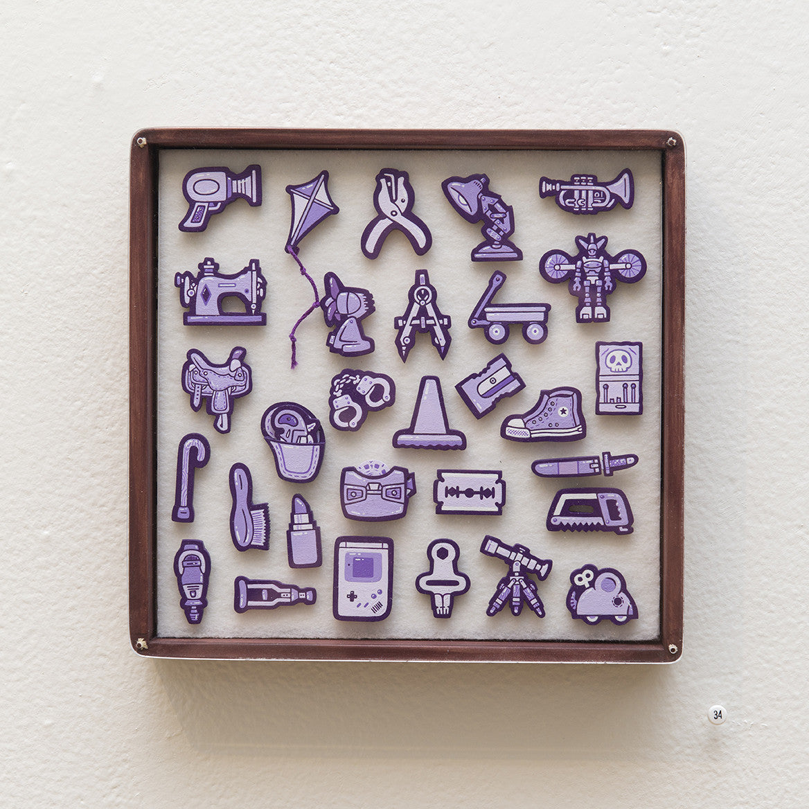 Matt Ritchies wooden-framed Tiny Objects display features purple, textured acrylic cutouts of a camera, kite, scissors, and sewing machine on a white background. Each is crafted from hand-cut wood and includes a small label numbered 34 at the bottom right.