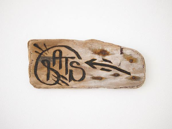 A GATS rustic wooden sign with black graffiti-style text and a right-pointing arrow is mounted on a white wall, its wood resembling burnt driftwood for added worn charm.