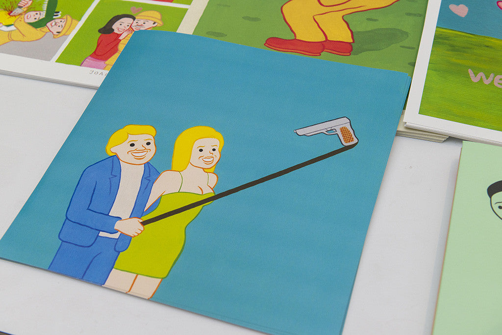 A Joan Cornellà-style digital print features two people smiling and using a mop as a selfie stick, part of a colorful art collection displayed on a white surface.