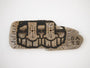 A wooden piece of burnt driftwood with carved, stylized three-eyed faces and intricate linework features the inscription GATS on the right side. This striking wood burn art is influenced by urban and tribal motifs.