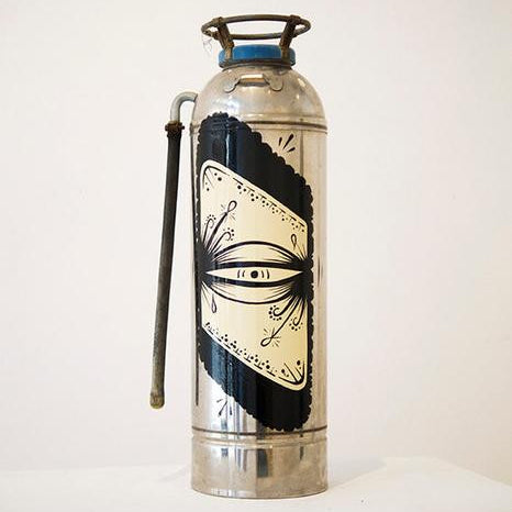 The GATS vintage silver fire extinguisher with a stylized eye design and black and white detailing stands elegantly on a clean, white surface, featuring an enamel finish that adds sophistication against the plain background.