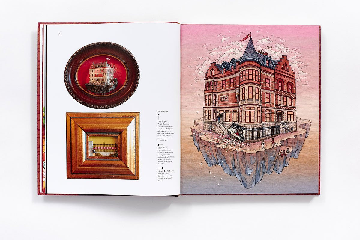 An open book showcases two pages. The left side displays framed miniature building dioramas in Wes Andersons style, while the right features a detailed floating mansion illustration with nearby figures, all echoing Spoke Art Gallerys Bad Dads exhibition by Matt Zoller Seitz.