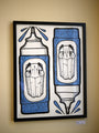 A framed GATS artwork features two tribal art-inspired marker pens with intricate blue patterns and black and white faces on the tips, resembling a GATS print. This limited edition piece contrasts beautifully against its simple, pale background.