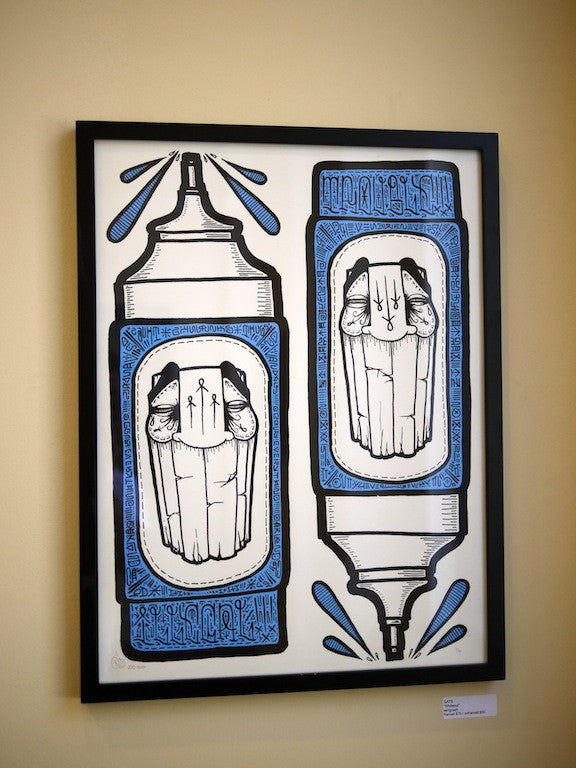 A framed GATS artwork features two tribal art-inspired marker pens with intricate blue patterns and black and white faces on the tips, resembling a GATS print. This limited edition piece contrasts beautifully against its simple, pale background.