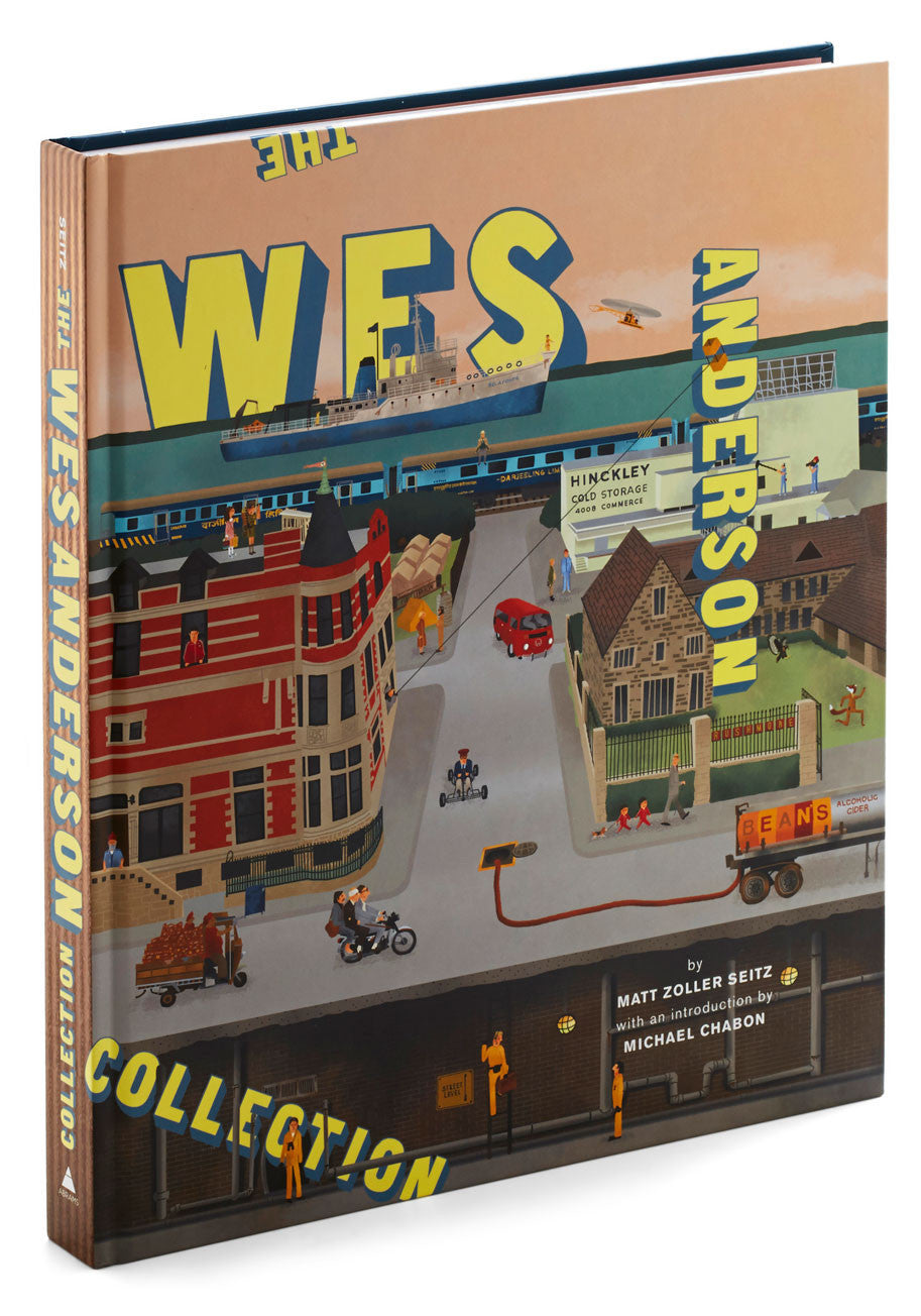 The cover of Matt Zoller Seitzs The Wes Anderson Collection showcases a stylized town scene with a train, buildings, and people. The title stands out in large, colorful lettering, providing insight into Andersons films.
