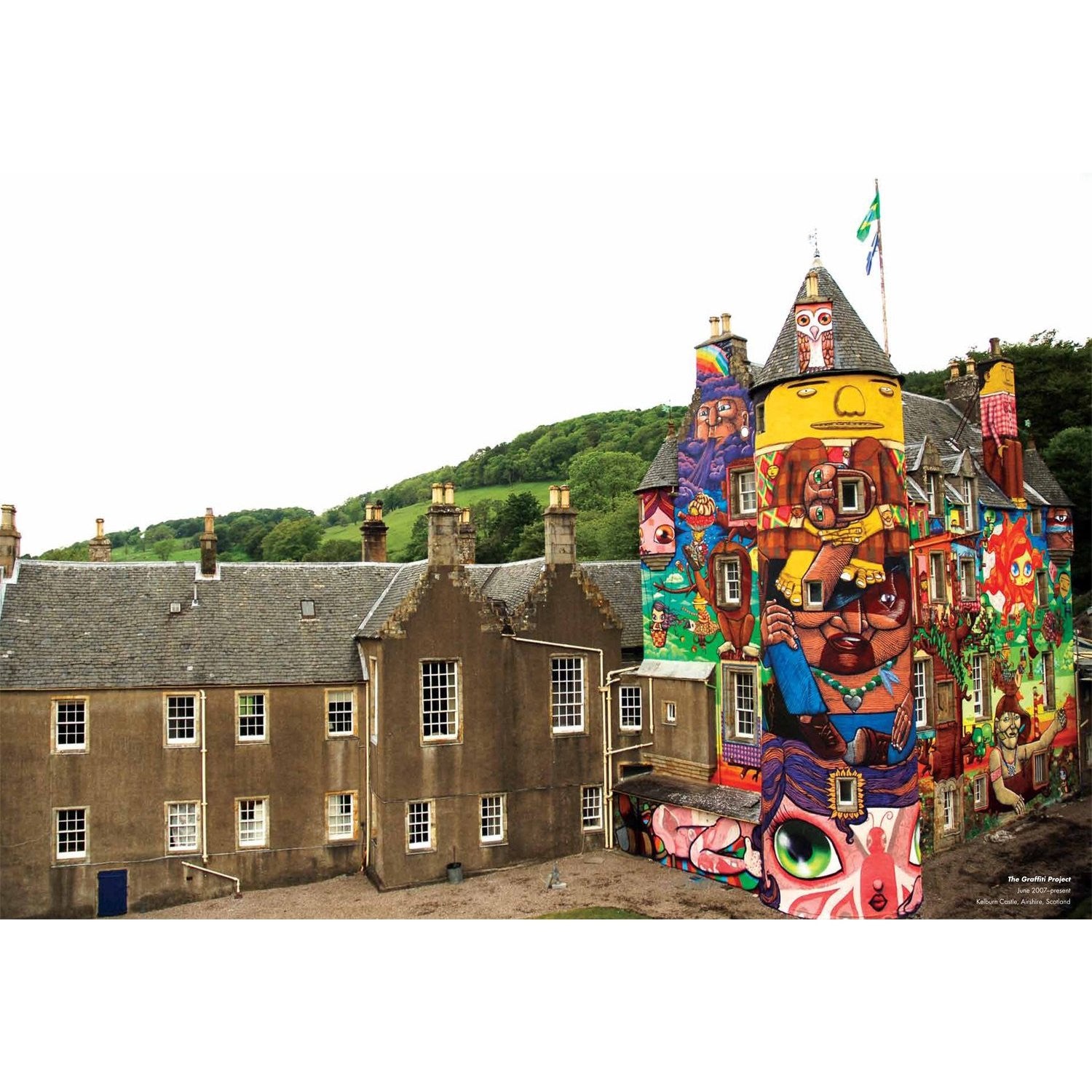 A historic building with traditional architecture is vibrantly painted in colorful urban art and murals. The artwork, echoing the Os Gemeos style, contrasts modern designs against the classic stone structure, while green hills in the background enhance this striking graffiti scene.