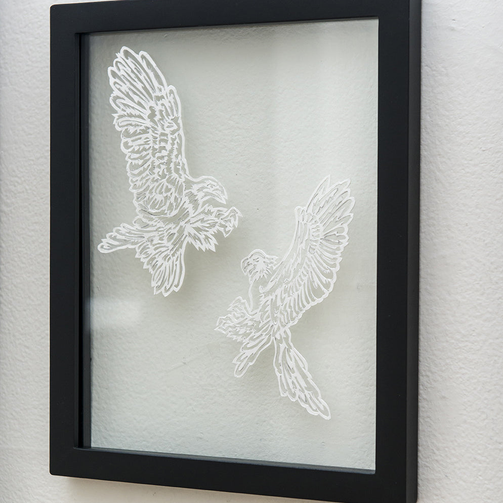 A framed art piece by Elaine Penwell showcases two intricately hand-cut paper birds titled Flight Call, facing each other with wings spread wide, set against a plain background within a sleek black frame.