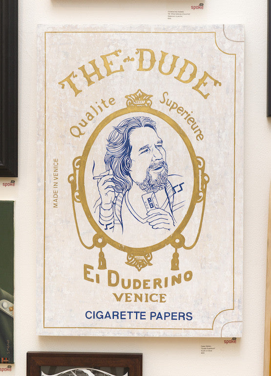 A Casey Weldon-inspired art poster titled The Dude showcases a bearded man with a card and cigarette. Styled as a vintage rolling paper pack, it features Qualite Superieure, El Duderino, and Cigarette Papers.