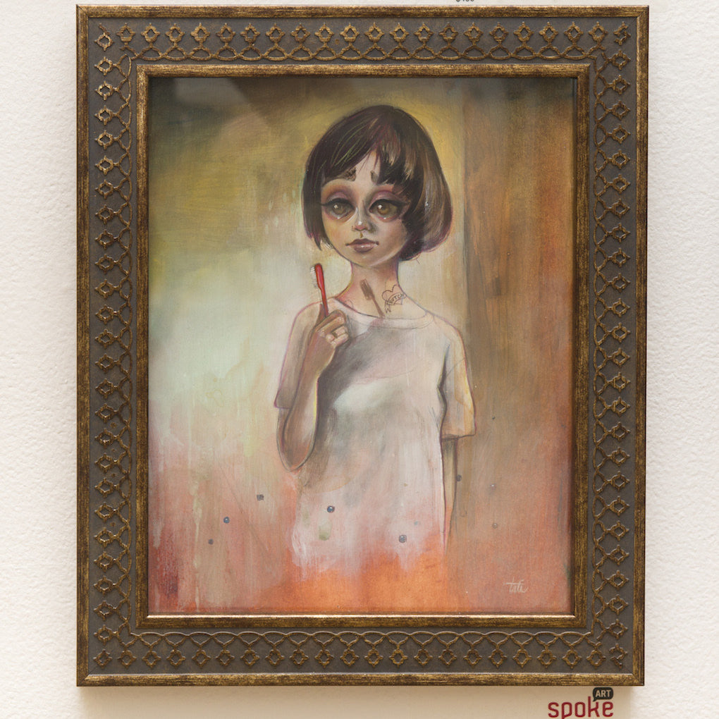 A framed Tatiana Suarez painting features a young person with short dark hair and big eyes, holding a red stick against a warm-hued background. Titled Merde! You Startled Me, its showcased on a white wall with price tags below.
