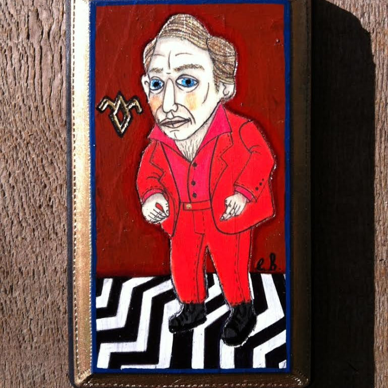 A stylized mixed media painting by Evan Harris depicts a man in a red suit with blue eyes on a zigzag black-and-white floor, against a deep red background featuring a strange symbol. It is framed in gold on wood, reminiscent of an exhibit at Spoke Art Gallery.