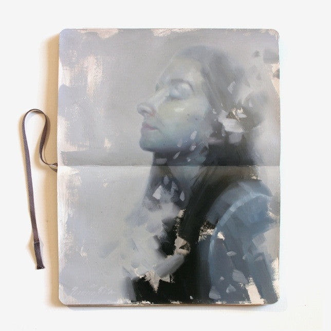 An open sketchbook displays an oil on moleskine portrait in the style of Henrik Uldalen. The grayscale image features soft, dreamy tones and closed eyes, with an abstract blend and a ribbon bookmark on the left, evoking Last Caress..