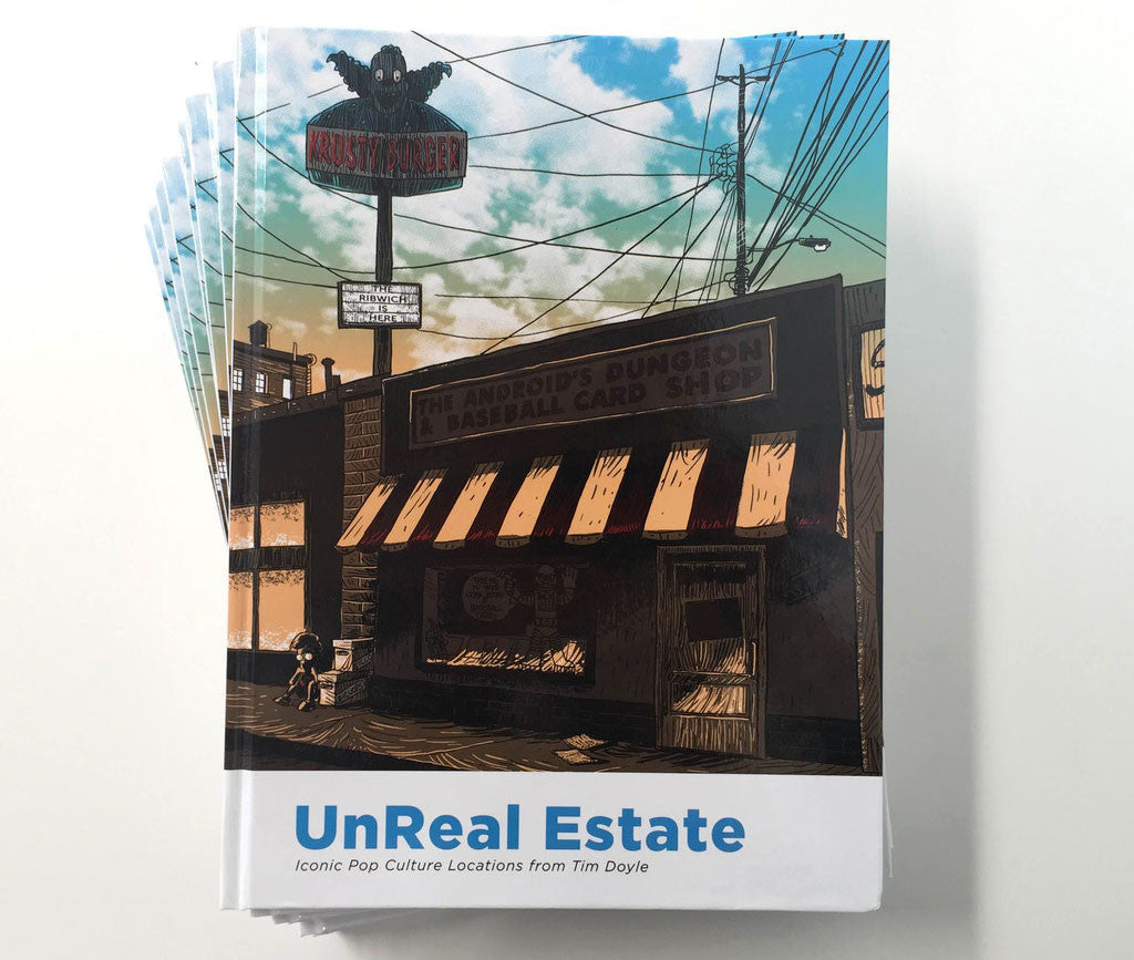 The image shows Tim Doyles hardcover book UnReal Estate: Iconic Pop Culture Locations. The cover features a comic-style illustration of The Androids Dungeon & Baseball Card Shop.