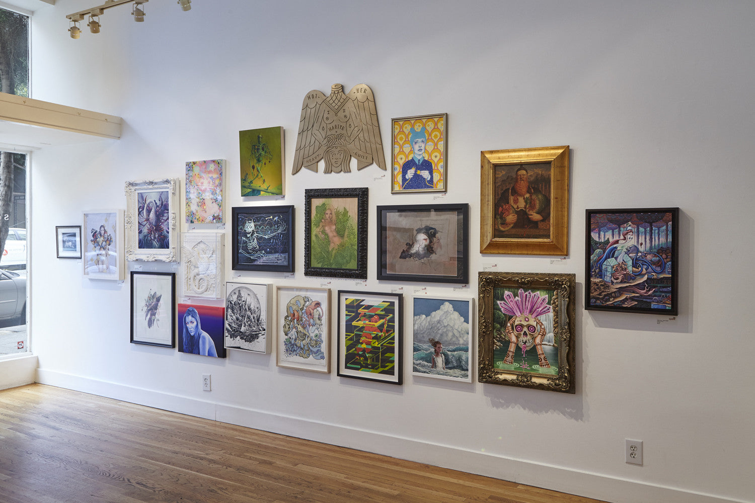 A gallery wall displays framed artworks, including Inkys Demise pieces, in a grid. An eagle sculpture is at the center. The room, reflecting Scott Teplins style with wooden floors and a window on the left, enhances the collections allure.