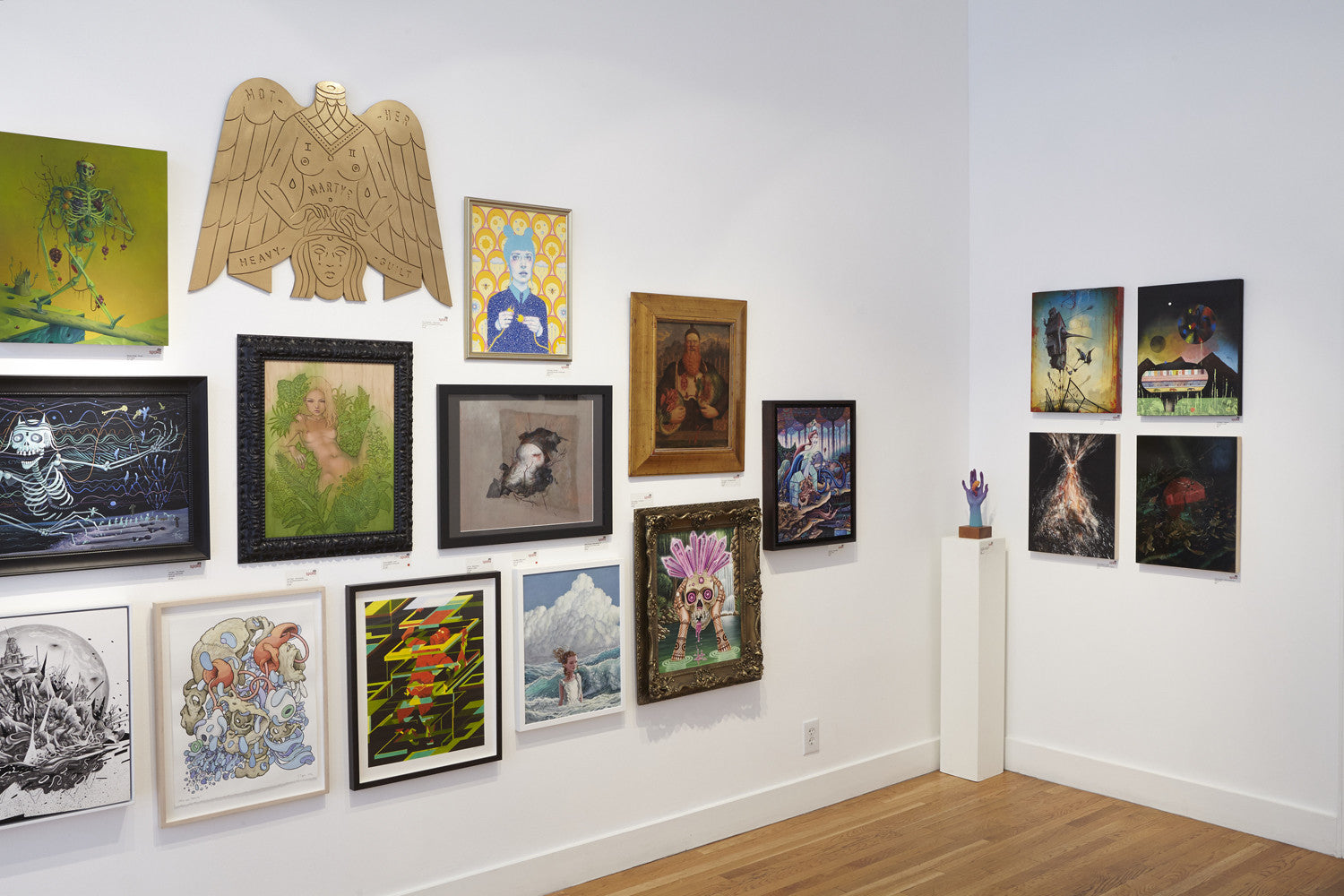 The salon-style gallery wall features a vibrant mix of framed paintings and illustrations, highlighted by a piece from Suggestivism: Resonance by Scott Teplin. A small sculpture on a pedestal nearby enhances the depth of this diverse collection.