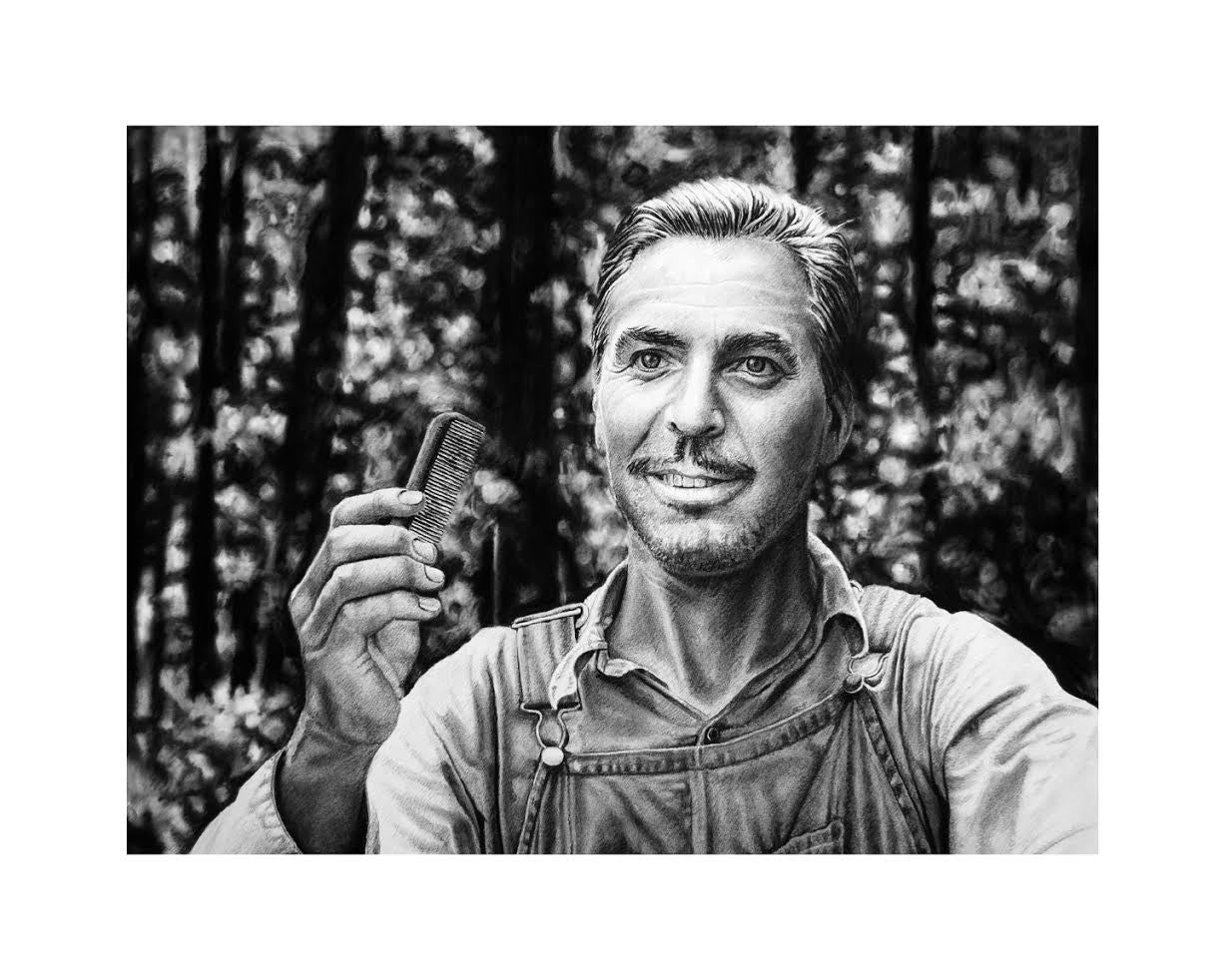 A grayscale image of a man outdoors, wearing a buttoned shirt under overalls and holding a small comb in his right hand while smiling slightly. Blurred trees suggest a forest setting. This Joel Phillips archival pigment print comes custom framed to enhance its charm.