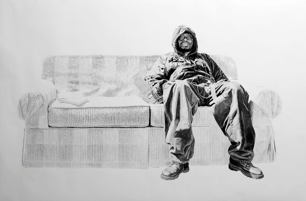 A man in a hooded jacket and baggy pants relaxes on a partially sketched couch. Rendered with charcoal and graphite, the black-and-white background contrasts the grayscale details of the man. A book or magazine lies beside him, echoing Joel Phillips art seen at San Francisco fairs.