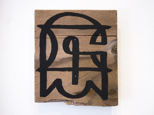 A wooden plank featuring abstract black graffiti in GATS style, crafted with acrylic paint, showcases geometric shapes and stylized lines on a white background.