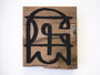 A wooden plank featuring abstract black graffiti in GATS style, crafted with acrylic paint, showcases geometric shapes and stylized lines on a white background.