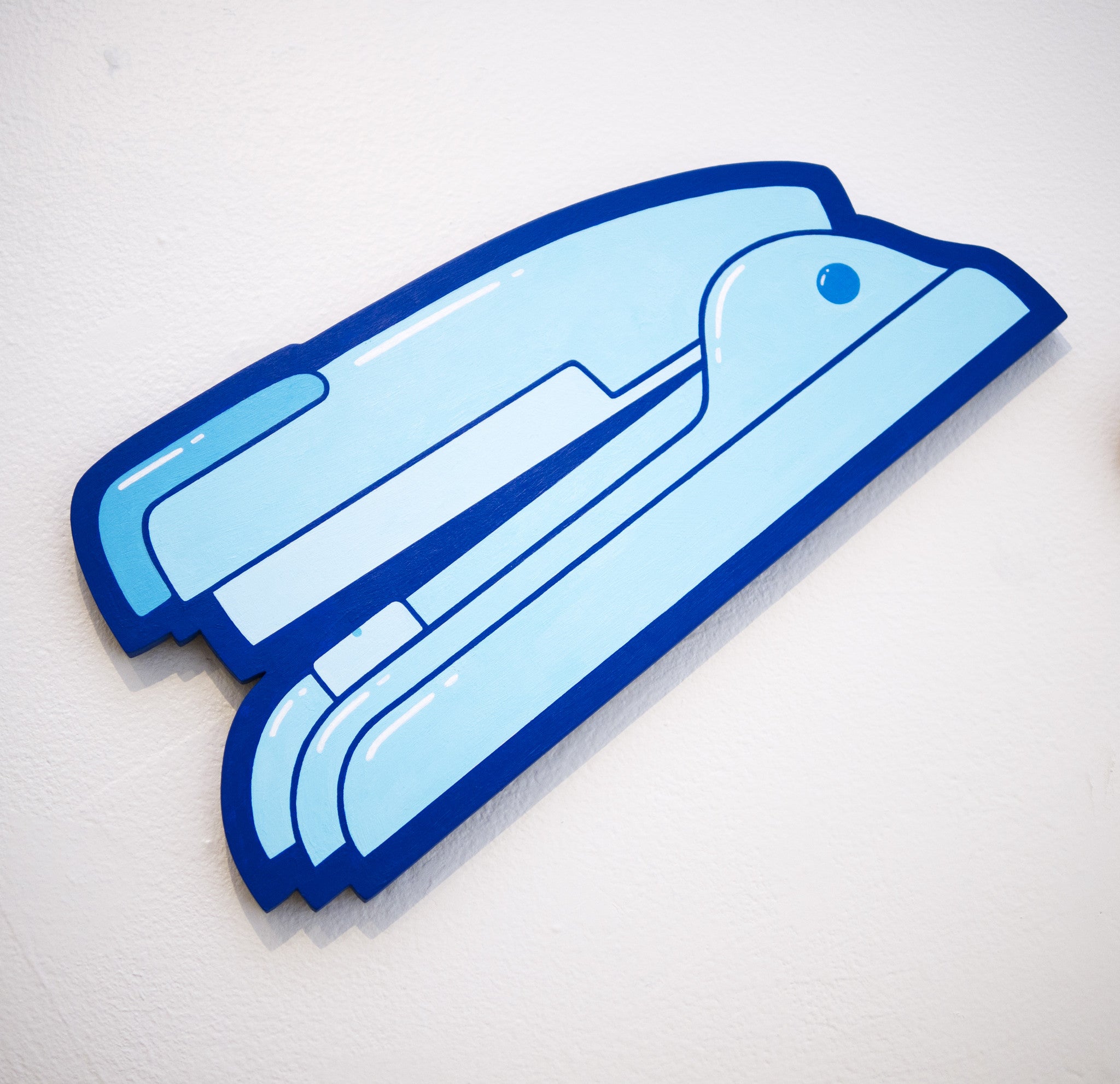 A bold, graphic-style illustration in Matt Ritchie fashion features a light blue stapler with dark blue outlines against a neutral wall, evoking the tactile feel of hand-cut wood.
