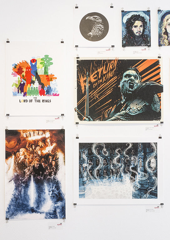 A wall showcases James R. Eads-inspired fantasy art prints, with archival pigment pieces echoing his whimsical style. Colorful illustrations highlight mythical figures and creatures with nods to franchises like the Hall of Faces, each artwork neatly clipped on display.