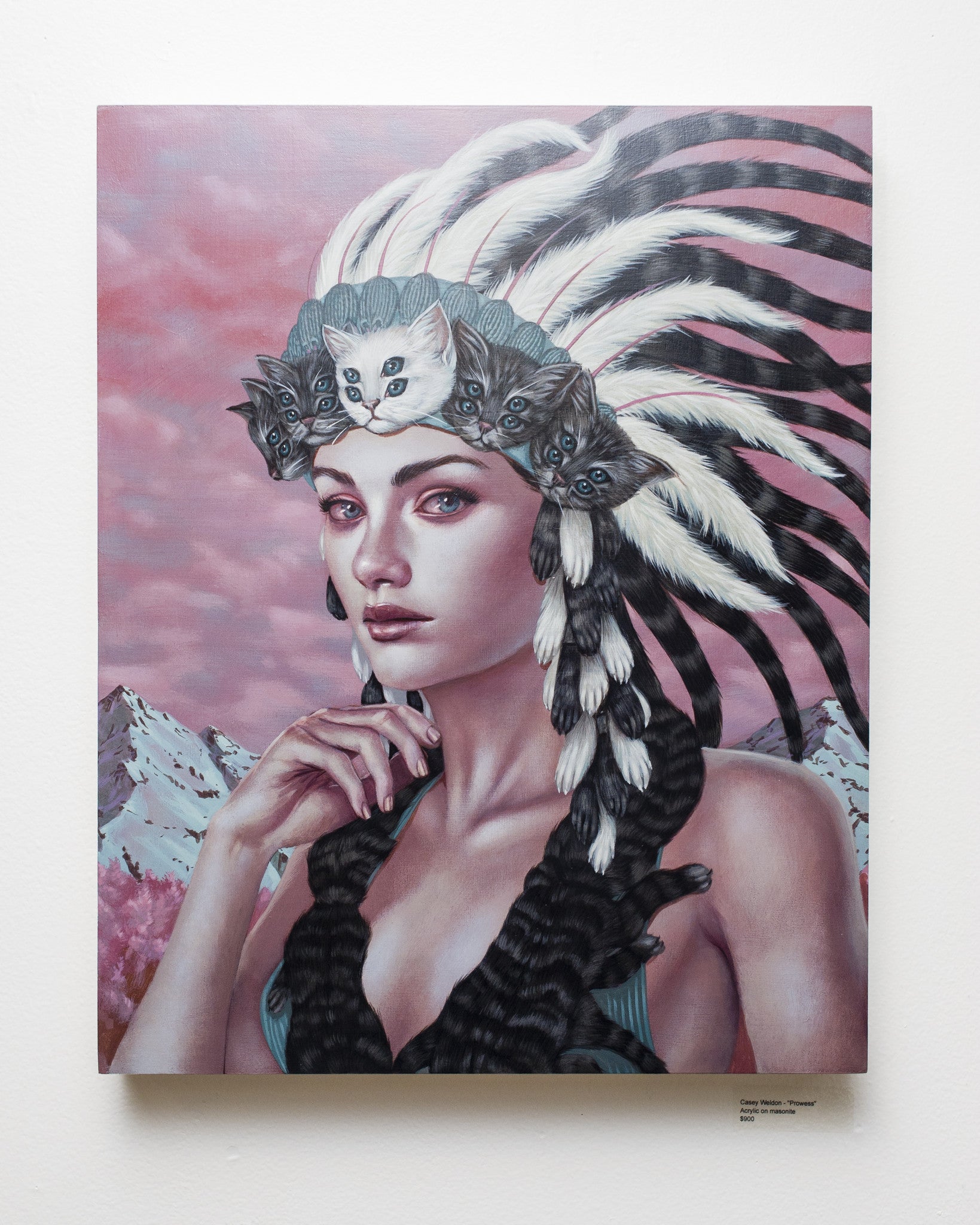 In Casey Weldons Prowess, a woman wears a feathered headdress with a cat face, her long braids enhancing her look. The acrylic on masonite artwork depicts mountains beneath a pink sky, merging surreal beauty with intricate detail.