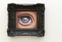 An ornately framed painting by Ana Bagayan, depicts a skeleton eye with a purple iris featuring a tiny skull. The dark, intricate frame complements the artworks mysterious theme perfectly.